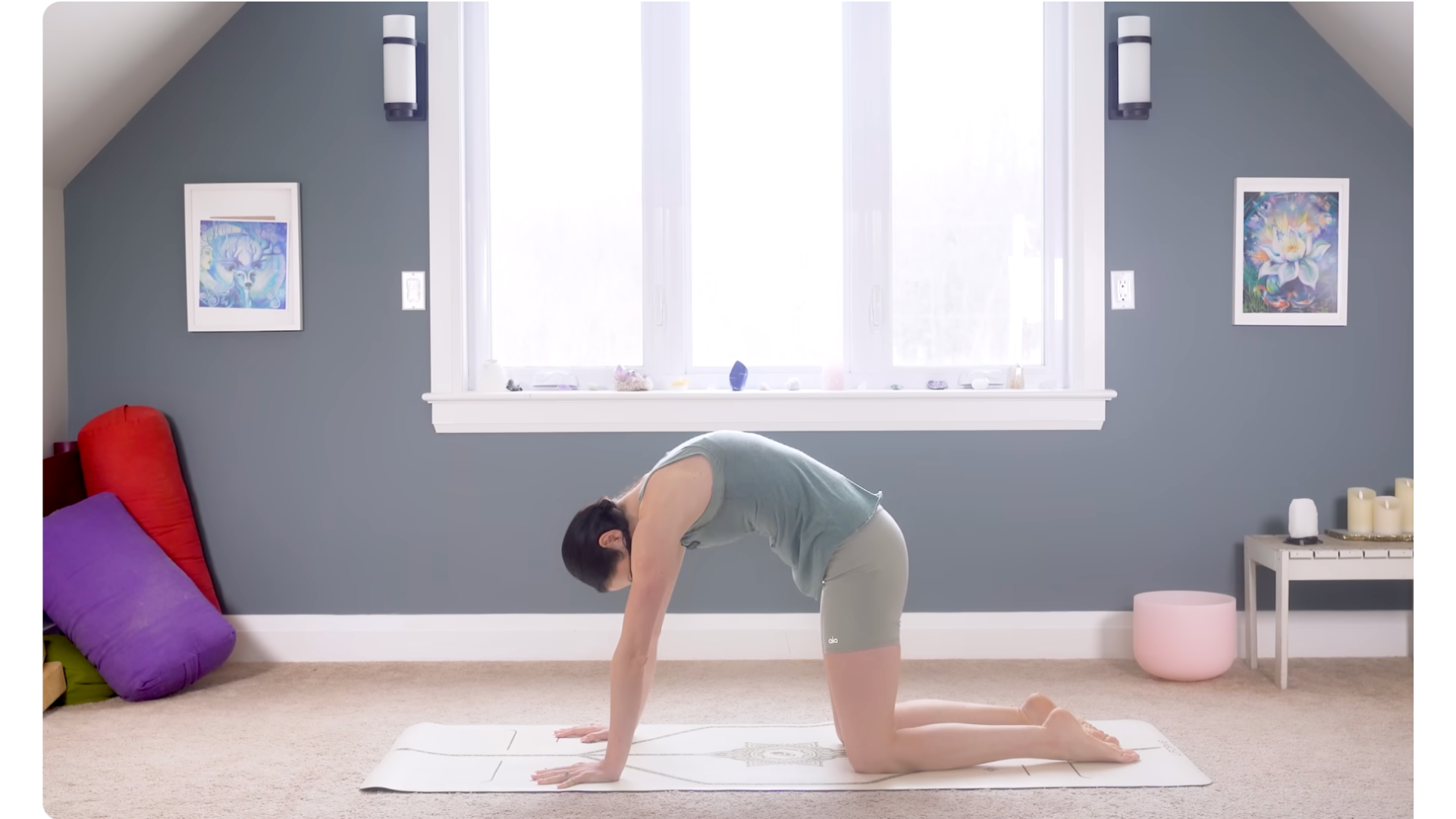 Yoga teacher on hands and knees practicing Cat Pose by rounding her back